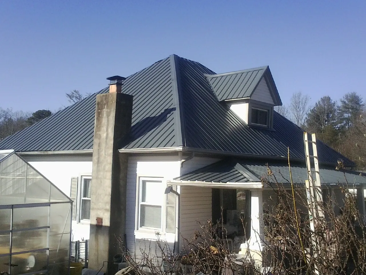 Dark blue standing seam metal roof on a white farmhouse with dormer — Slate & Tile Roof Repair by Roofing Brothers in Morehead City