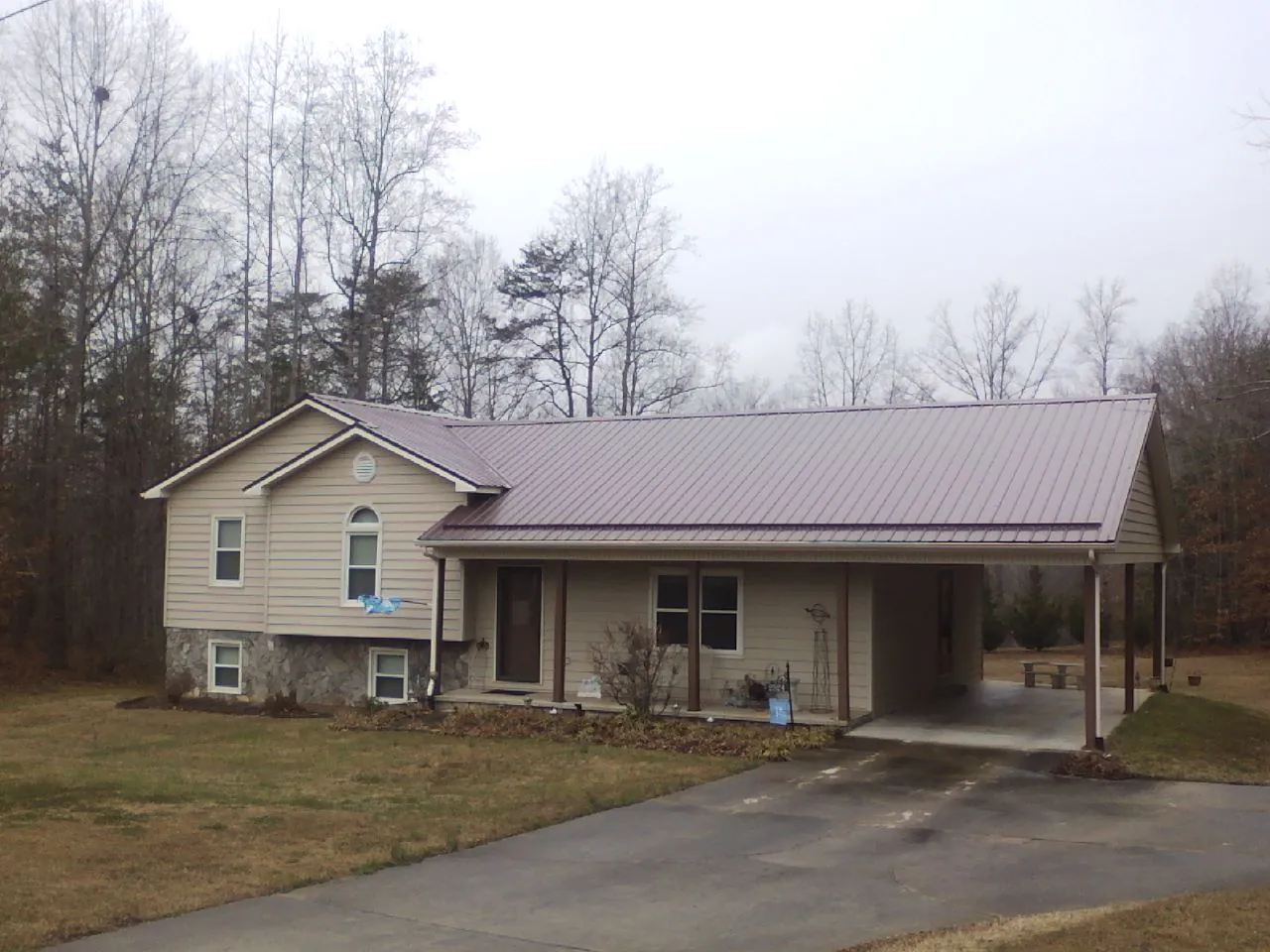 Burgundy metal roof on a tan split level home with an attached carport in Morehead City