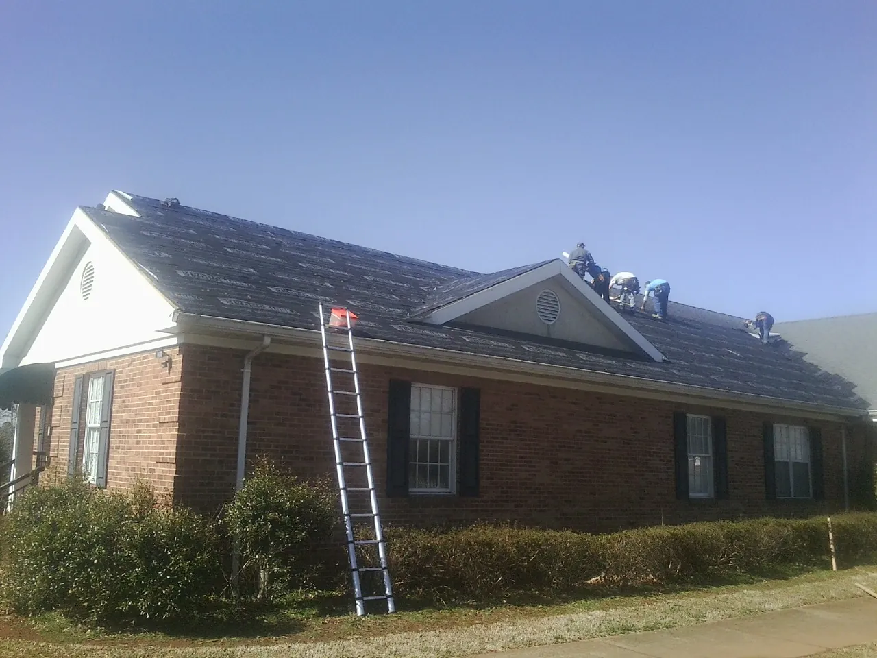 Crew tearing shingles off a brick ranch roof with a ladder set — Metal Roof Repair work by our crew in Morehead City
