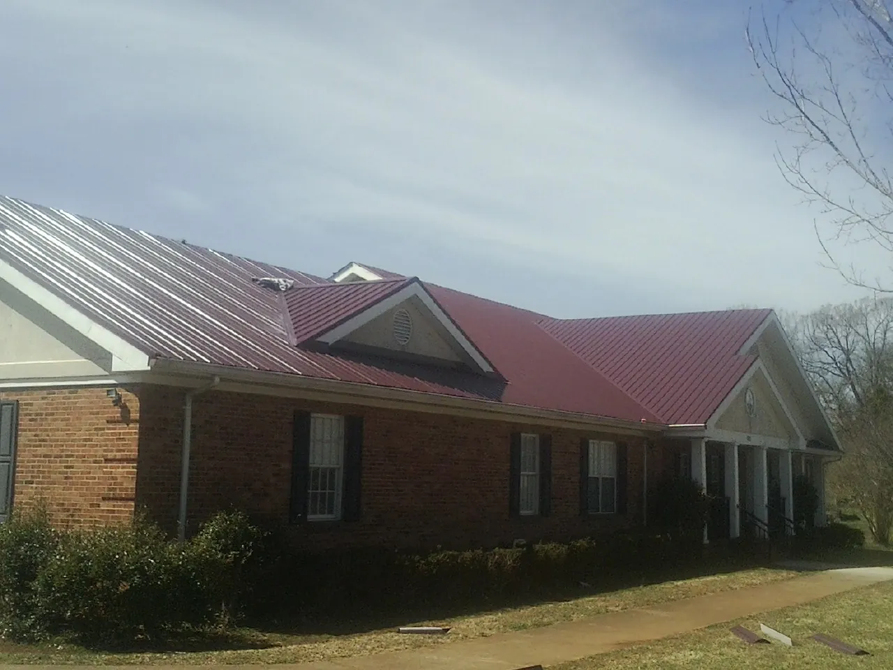 Red metal roof with gabled entries on a long brick building, from a Hail Damage Roof Repair job in Morehead City