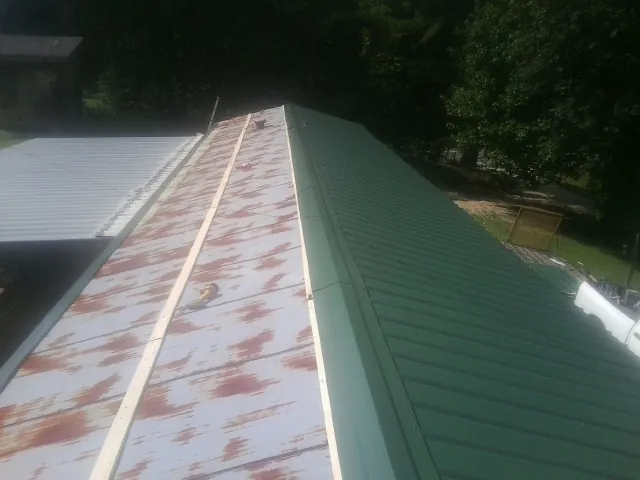 Old rusted panels beside newly installed green metal roofing — Wind Damage Roof Repair by Roofing Brothers in Morehead City