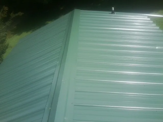 New green metal panels meeting at the ridge of a roof — Flat Roof Repair work by our crew in Morehead City