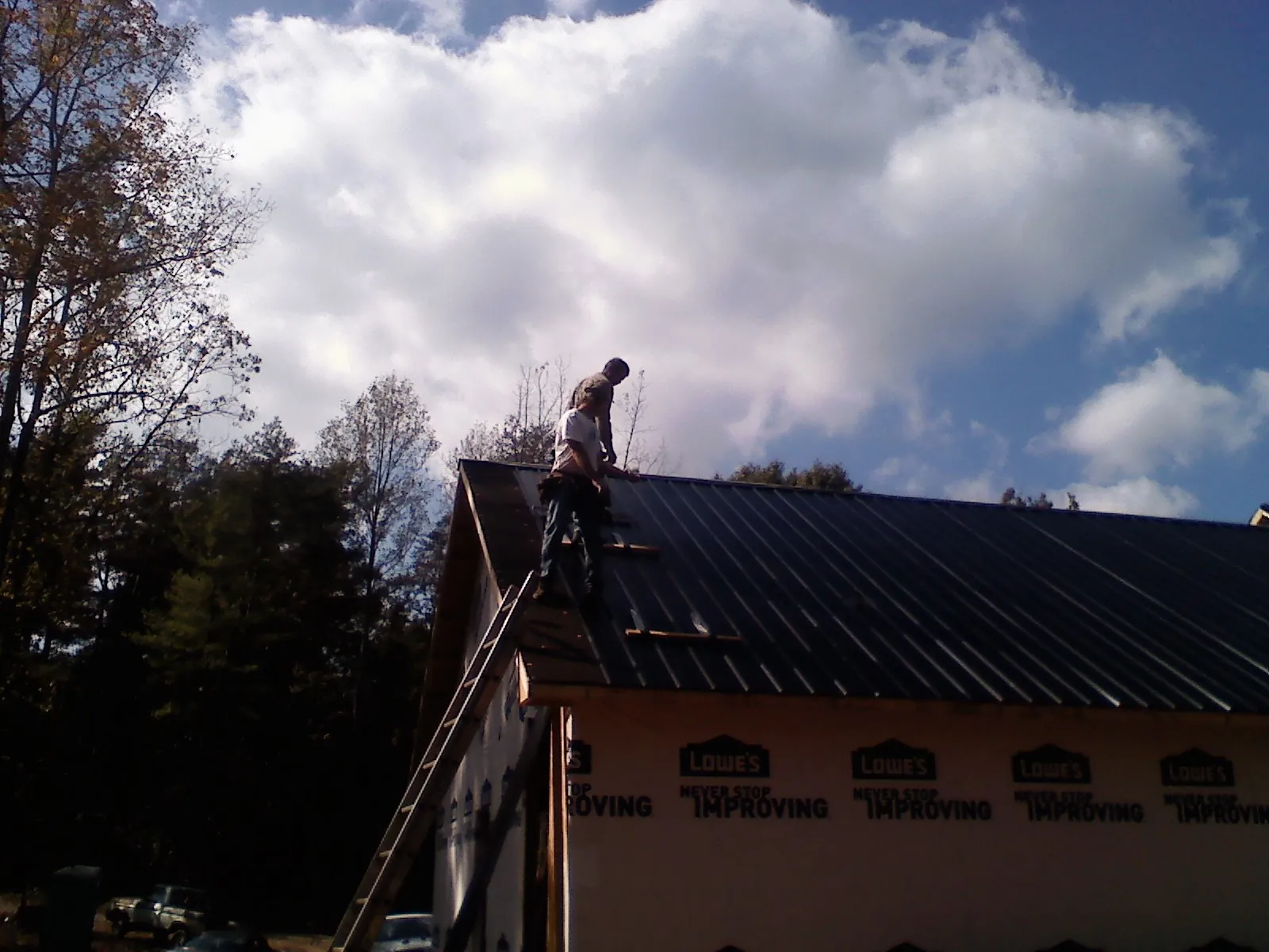 Roofer fastening dark metal panels high against a cloudy sky, from a Roof Inspection job in Morehead City