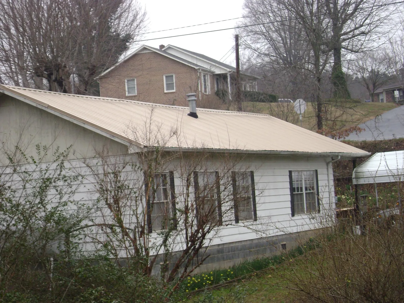 Tan metal roof on a white sided house set into a hillside — Commercial Roofing by Roofing Brothers in Morehead City