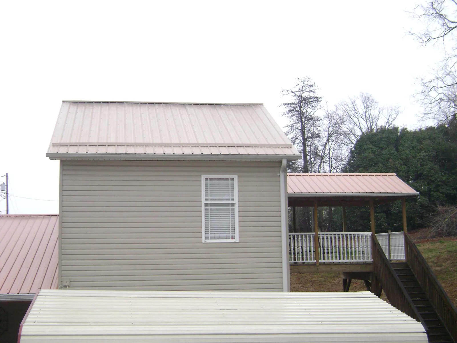 Tan metal roofs on a two story addition and attached porch, from a Roof Replacement job in Morehead City