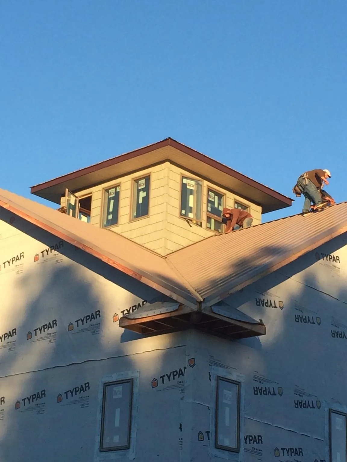 Roofers working around a rooftop cupola on a new metal roof at sunset — Roof Waterproofing in Morehead City by Roofing Brothers